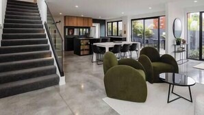 A modern interior with a staircase, a dining area, and a seating area with green chairs. - The Buller St Retreat (New Plymouth)