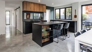 A modern kitchen with a central island, bar stools, and a dining area with a table and chairs. - The Buller St Retreat (New Plymouth)