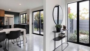 A modern kitchen with a dining area, large windows, and a black metal shelf with a plant. - The Buller St Retreat (New Plymouth)