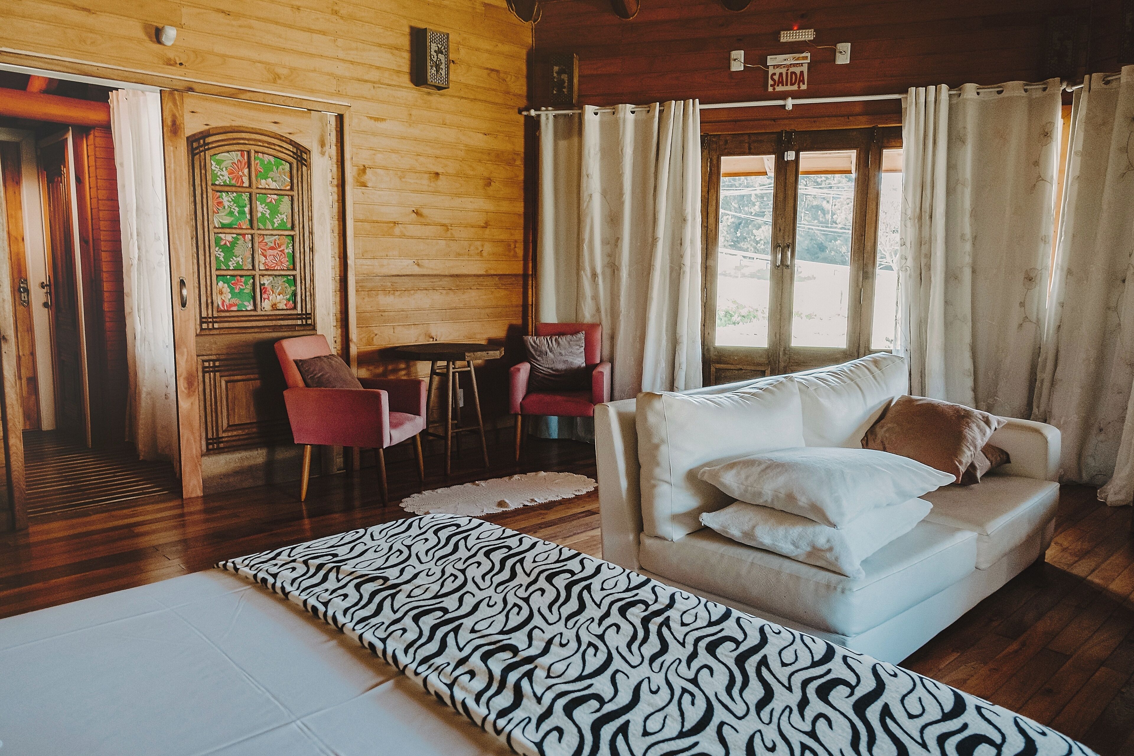 A cozy room with a wooden interior, a white sofa with pillows, a zebra-patterned rug, and a window with curtains.
