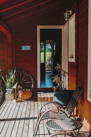 A wooden porch with a rustic aesthetic, featuring a large wheel, potted plants, and a metal chair. - Pousada Caminhos de Mel - Urubici - SC (Urubici)