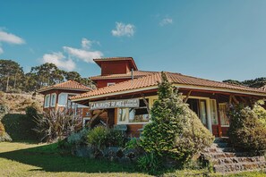 A two-story house with a tiled roof, a sign reading "Caminhos Du Mel Familia Barbezuan," and a stone staircase leading to the entrance. - Pousada Caminhos de Mel - Urubici - SC (Urubici)