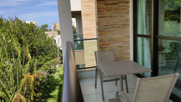 A balcony with a table and chairs, overlooking a garden and neighboring buildings. - ILOA: Conforto, Natureza e Lazer (Barra de São Miguel)