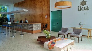 A modern reception area with a wooden reception desk, a green door, and a seating area with a table and chairs. - ILOA: Conforto, Natureza e Lazer (Barra de São Miguel)