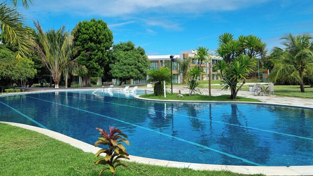 A swimming pool with clear blue water, surrounded by lush green grass and palm trees. - ILOA: Conforto, Natureza e Lazer (Barra de São Miguel)