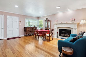 A living room with hardwood flooring, a blue sofa, a fireplace, and a dining area with a red tablecloth.