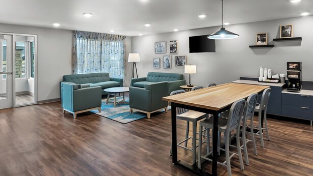 Un salon moderne avec un plancher en bois, deux canapés verts, une table basse et un coin repas comprenant une table en bois et des tabourets de bar.