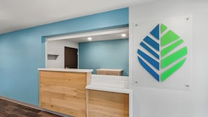 Un espace d’accueil avec un comptoir de réception en bois, un mur bleu et un logo affiché sur le mur.