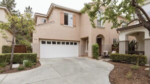 A residential house with a garage, a curved driveway, and a small patio area with a table and chairs. - Luxury Beach Home with Hot Tub
 (San Diego)