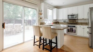 A modern kitchen with white cabinets, a granite countertop, and a central island with two bar stools. - Luxury Beach Home with Hot Tub
 (San Diego)