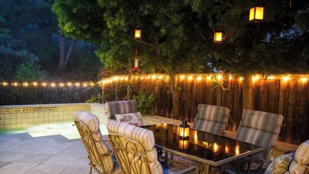 An outdoor patio with a pool, surrounded by wooden fencing and string lights. - Luxury Beach Home with Hot Tub
 (San Diego)