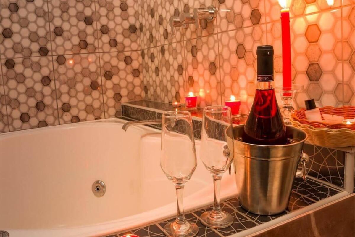 Una bañera con dos vasos y una botella de vino, velas y una cesta de toallas.