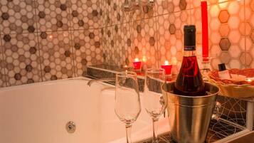 A bathtub with two glasses and a bottle of wine, candles, and a basket of towels.