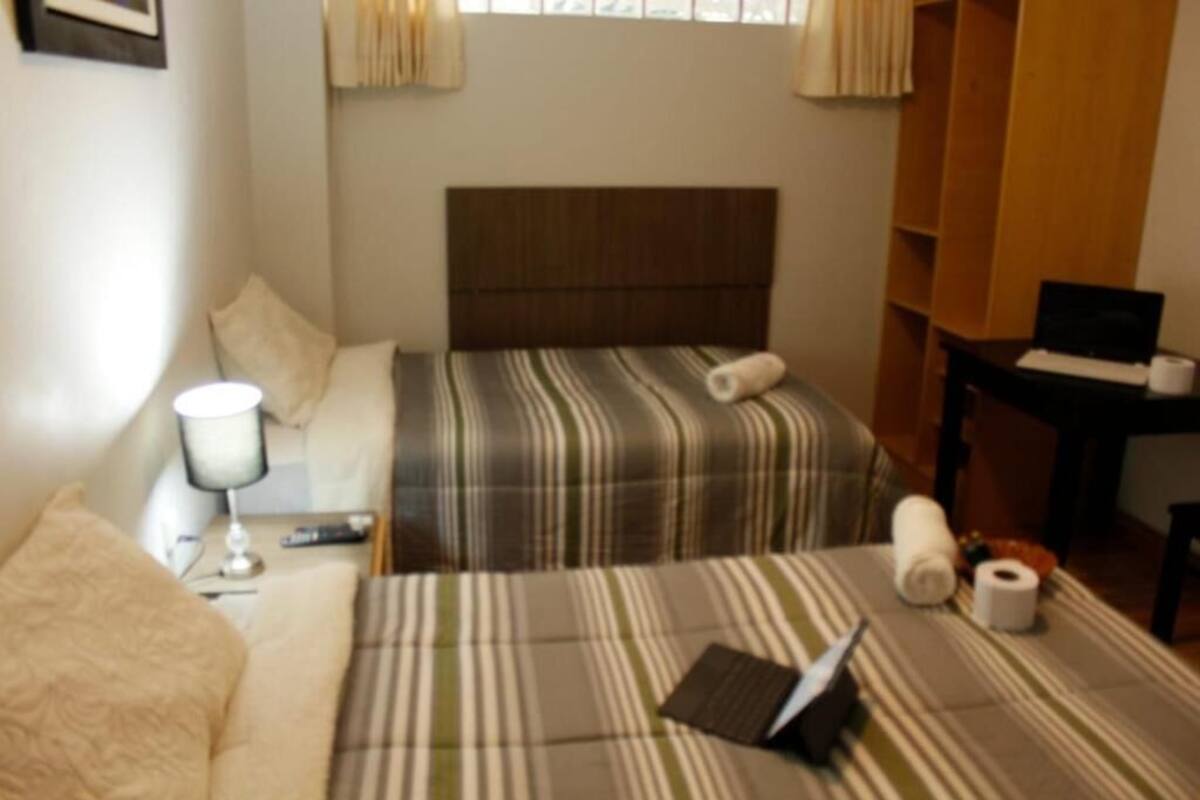 Una habitación de hotel con cama, escritorio, lámpara y ventana con cortinas.