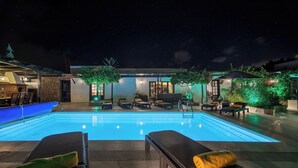 A swimming pool with lounge chairs and umbrellas, surrounded by a stone wall and greenery. - Private quiet villa with a short walk to beaches, restaurants, bars and shops. (Tías)
