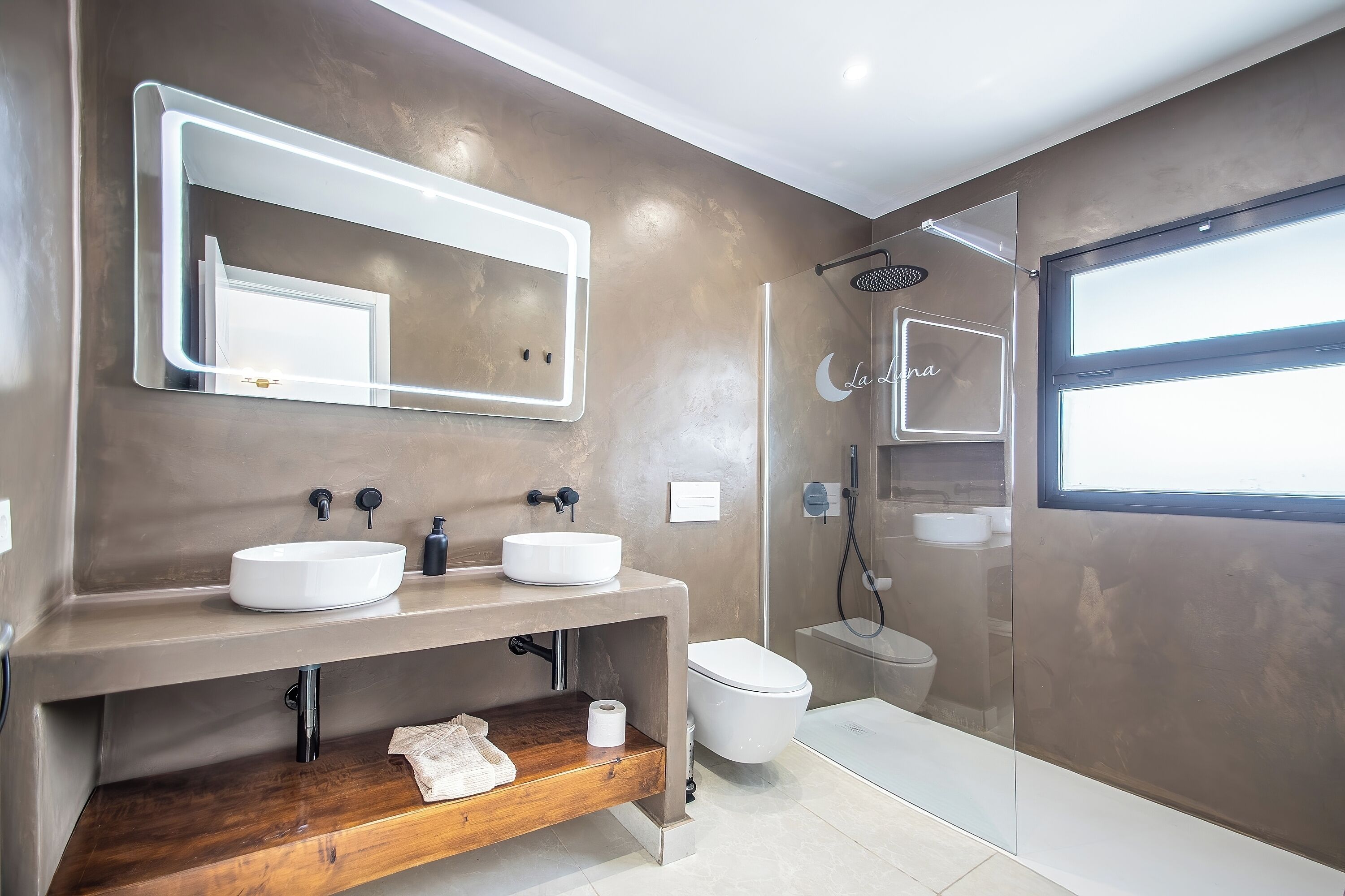 A modern bathroom with a large mirror, two sinks, a toilet, and a shower.