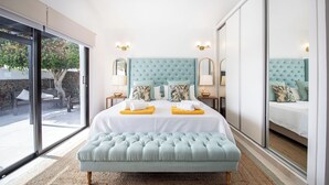 A bedroom with a large bed, a light blue upholstered bench, and a view through a sliding glass door to an outdoor area. - Private quiet villa with a short walk to beaches, restaurants, bars and shops. (Tías)