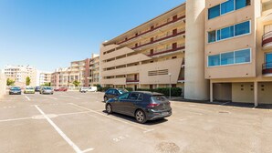 Un parking à étages où sont garées plusieurs voitures, situé à côté d’un immeuble doté de balcons et de grandes fenêtres.