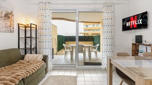 Un salon comprenant un canapé, une porte vitrée donnant sur une terrasse, un téléviseur fixé au mur et une table en bois.