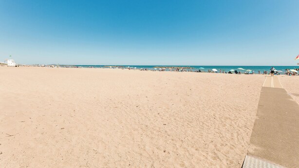 Une vaste plage de sable fin, un ciel bleu azur, quelques parasols et une côte lointaine.