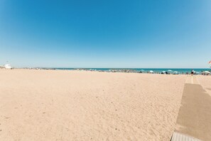 Ein weiter Sandstrand mit blauem Himmel, einigen Sonnenschirmen und einer fernen Küste.