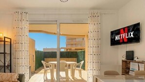 Un salon avec un canapé, un téléviseur fixé au mur et une table avec des chaises.