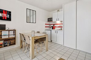 Moderni keittiö, jossa on valkoiset kaapit, mikroaaltouuni sekä ruokailutila, jossa on pöytä ja tuolit.
