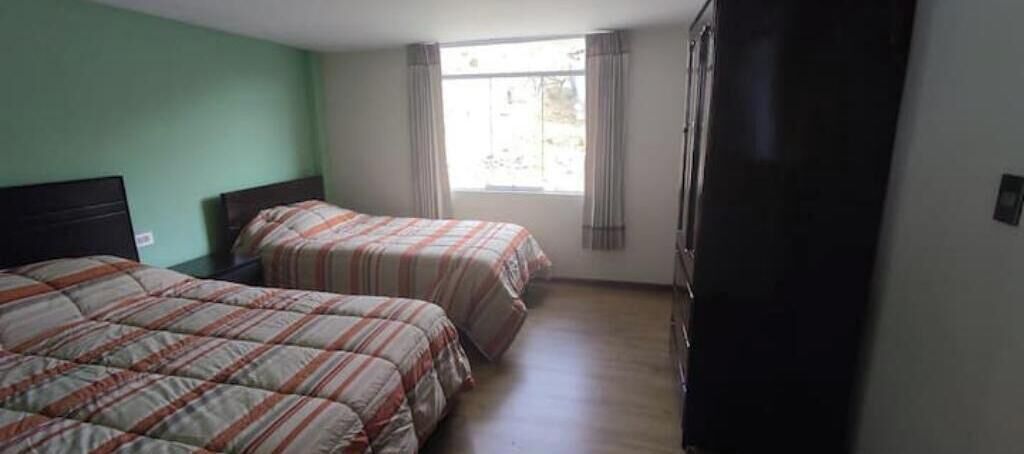 Una habitación con dos camas, una ventana con cortinas y un armario.