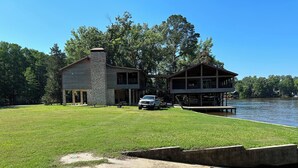 A two-story house with a stone chimney, a deck, and a dock extending into a lake. - House/Boat house on the river!  Boat lift and boat ramp, sun deck, ice machine (Karnack)