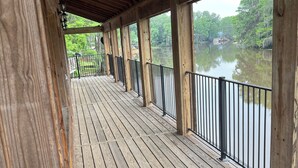 A wooden deck with railings overlooking a calm body of water, surrounded by trees. - House/Boat house on the river!  Boat lift and boat ramp, sun deck, ice machine (Karnack)
