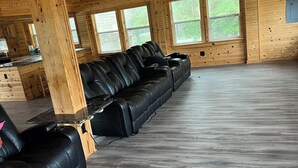 A spacious room with a long black leather sofa, wooden floors, and large windows. - House/Boat house on the river!  Boat lift and boat ramp, sun deck, ice machine (Karnack)