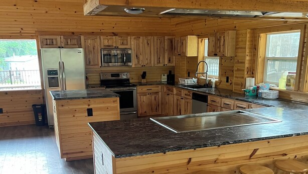 A spacious kitchen with wooden cabinets, a large island with bar stools, stainless steel appliances, and a view of the outdoors. - House/Boat house on the river!  Boat lift and boat ramp, sun deck, ice machine (Karnack)