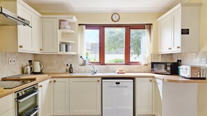 Una cocina con armarios blancos, lavavajillas, microondas, tostadora y ventana con cortinas.