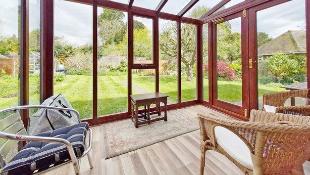 Un invernadero con techo de vidrio, muebles de mimbre, una pequeña mesa y vistas a un jardín.