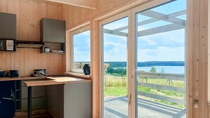 Eine moderne Küche mit Holzwänden, einem eingebauten Herd und einer großen Schiebeglastür, die auf eine Terrasse mit Seeblick führt.