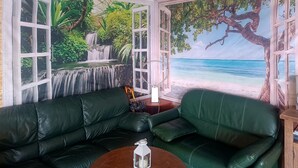 Ein Zimmer mit einem grünen Ledersofa, einem Holztisch und einem Wandbild mit einer Strandansicht.