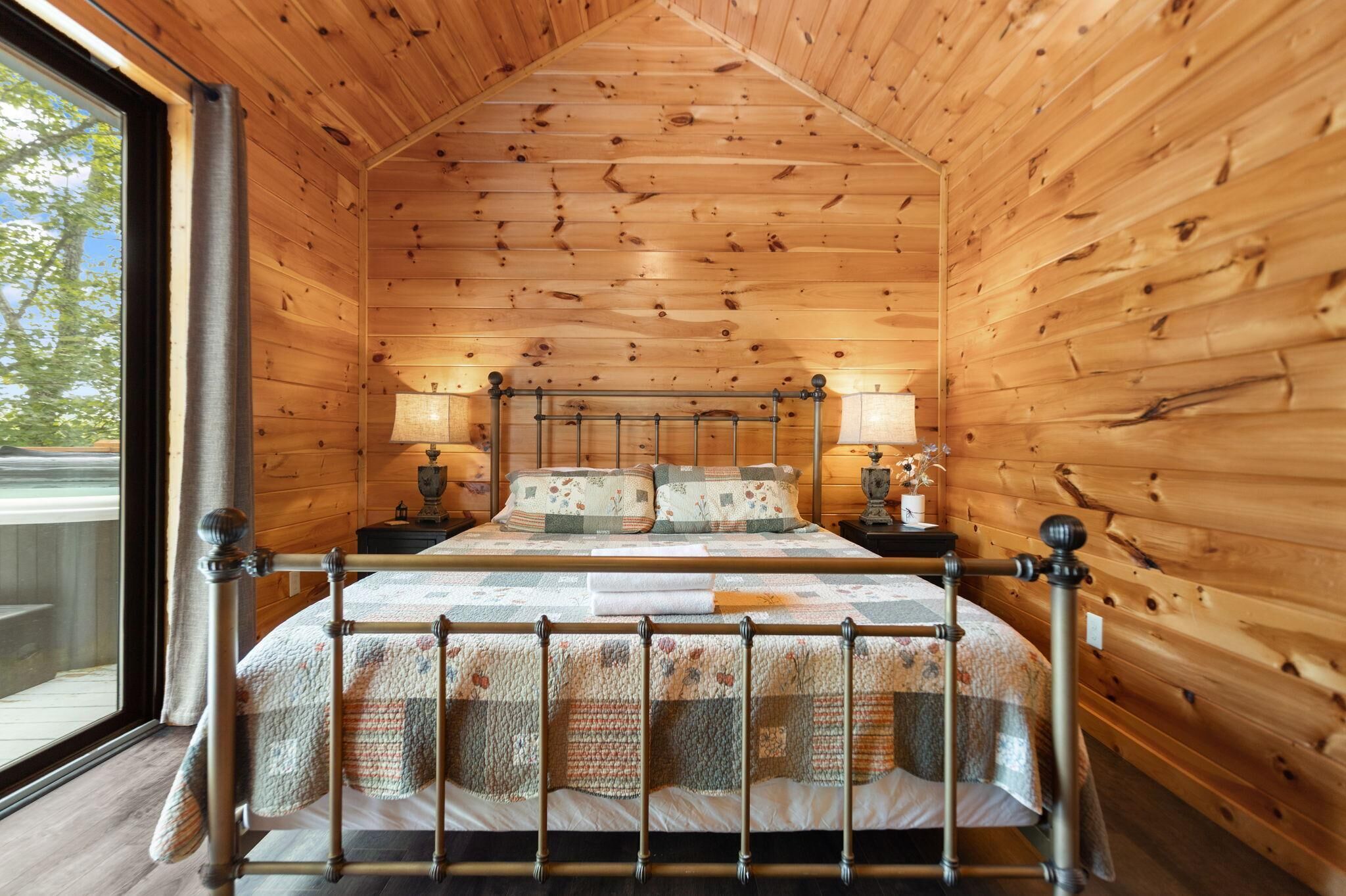 Un dormitorio de cabaña de madera con una cama, dos mesitas de noche y una ventana.