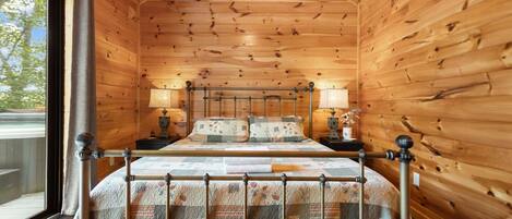 Un dormitorio de cabaña de madera con una cama, dos mesitas de noche y una ventana.