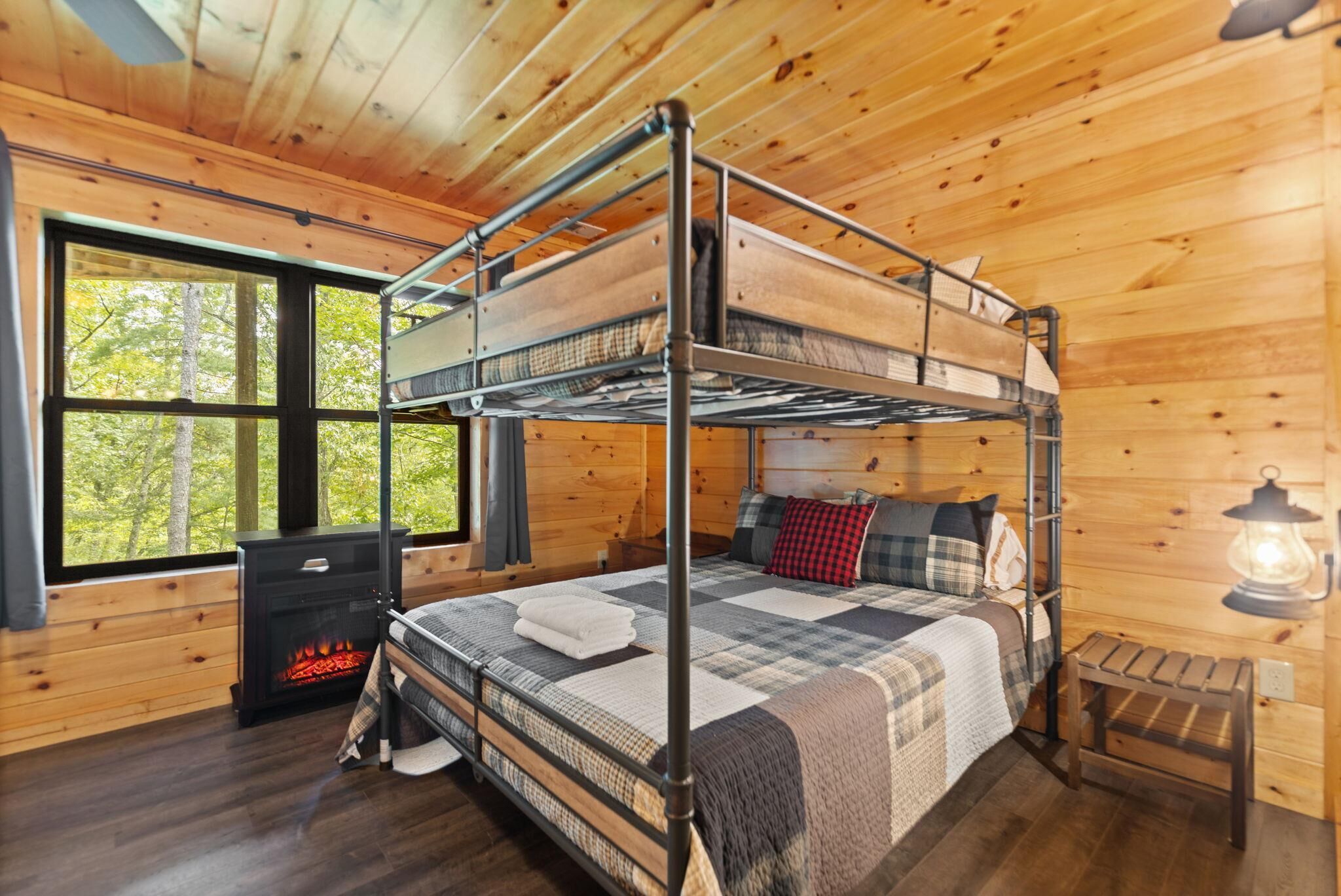A bunk bed room with a fireplace, wooden walls, and a large window.