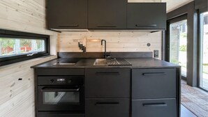 Une cuisine moderne avec des meubles de couleur sombre, un évier en acier inoxydable et une fenêtre donnant sur un jardin.