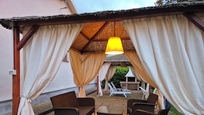 Un patio exterior con mobiliario de mimbre, una mesa y una estructura de techo de paja.