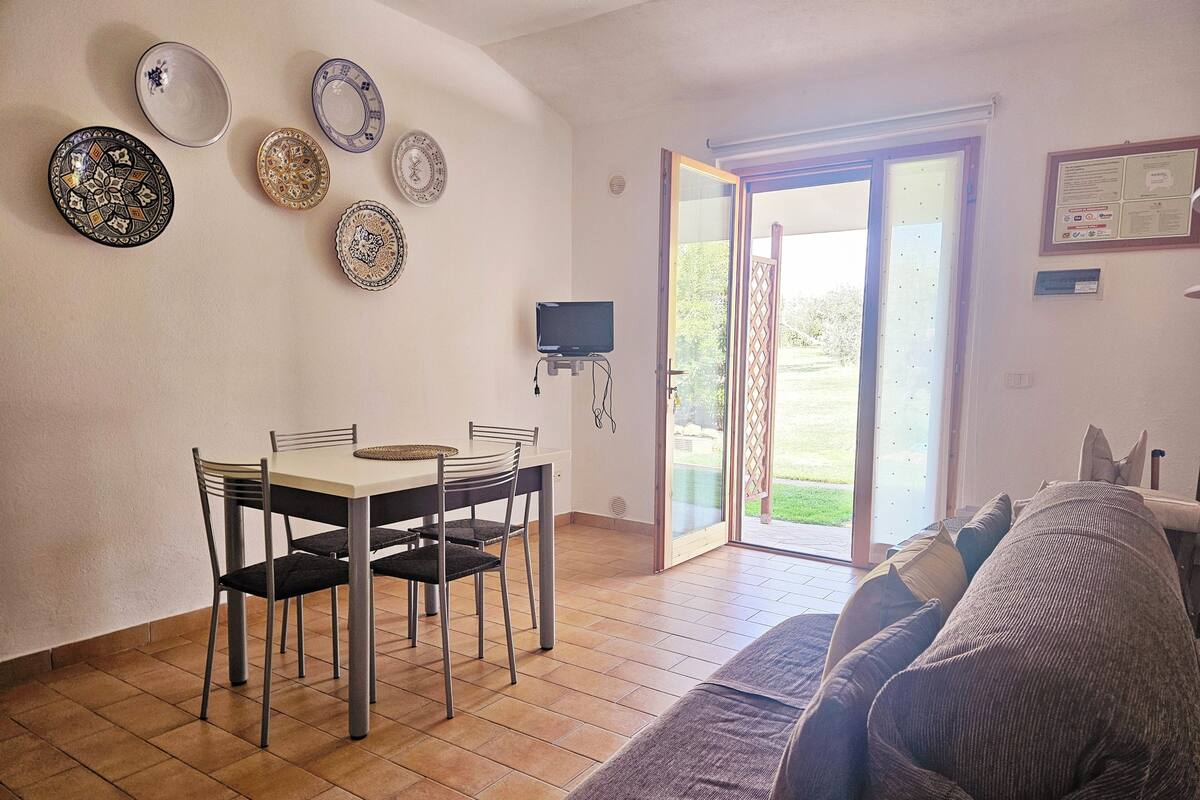 Ruokailutila, jossa on pöytä ja tuolit, sohva sekä seinälle asennettu televisio.