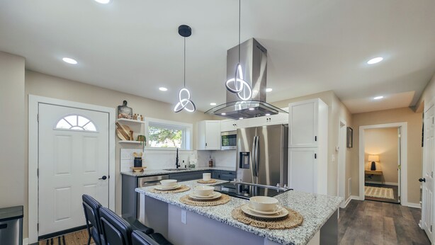Une cuisine moderne dotée d’un îlot central, d’appareils électroménagers en acier inoxydable et de luminaires suspendus.