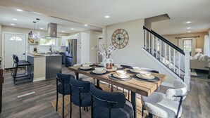 Une cuisine spacieuse équipée d’appareils modernes, un coin repas avec une table et des chaises en bois, et un escalier menant à l’espace de vie.
