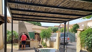 Eine Terrasse im Freien mit Steinboden, einem Tisch mit Glasplatte und Metallstühlen.