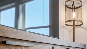 Un mueble de madera con varios cajones y un tirador metálico, ubicado cerca de una ventana con una lámpara de malla.