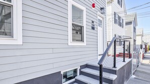 Un edificio residencial con fachada gris, detalles blancos y una ventana con un cartel de 'For Sale'.