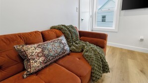 Una habitación con un sofá marrón, un cojín estampado y una manta verde.