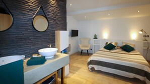 Una habitación de hotel moderna con un espejo grande y redondo, un lavabo blanco, un tocador de madera, una cama con ropa de cama a rayas y una silla.