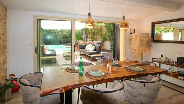Comedor con mesa de madera, sillas y vistas a una piscina y zona de estar al aire libre.